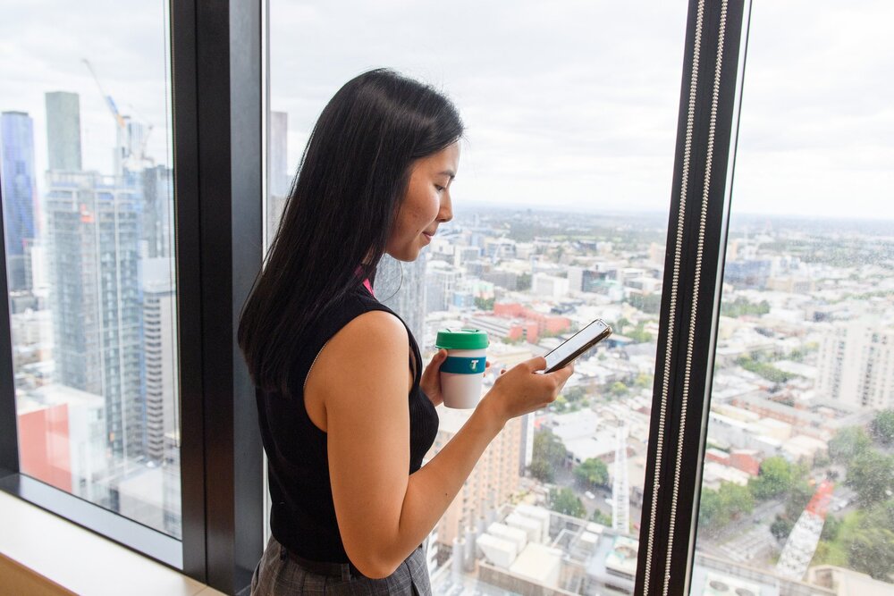 A young professional standing by her office window using her mobile phone