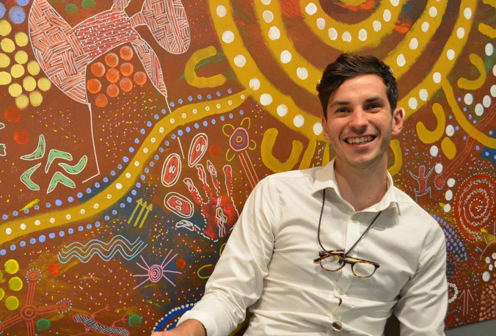 Beca Graduate- Young male professional sitting near wall full of colorful drawing..