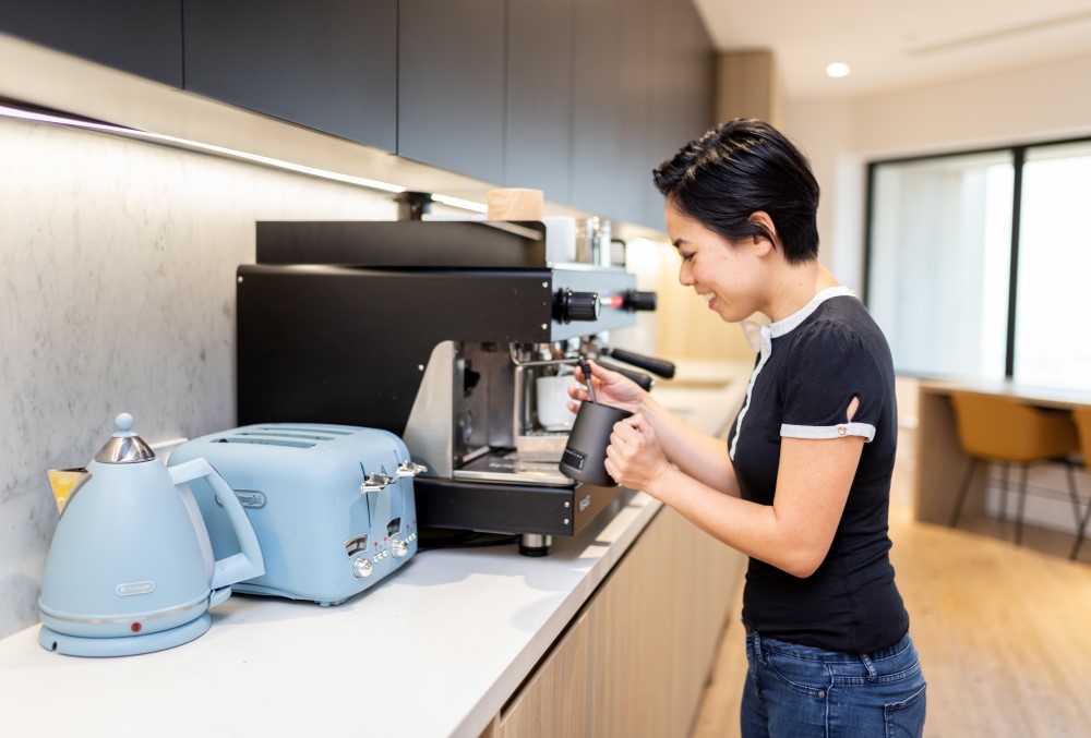 Exponential Trading Graduate- Young professional making coffee at the kitchen..